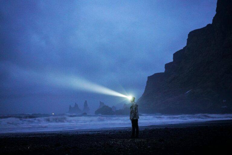 person with flashlight on beach at night